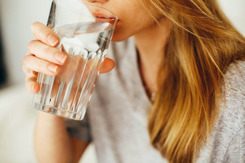 Žena pijúca pohár čistej vody, na doplnenie chýbajúcich tekutín v organizme.